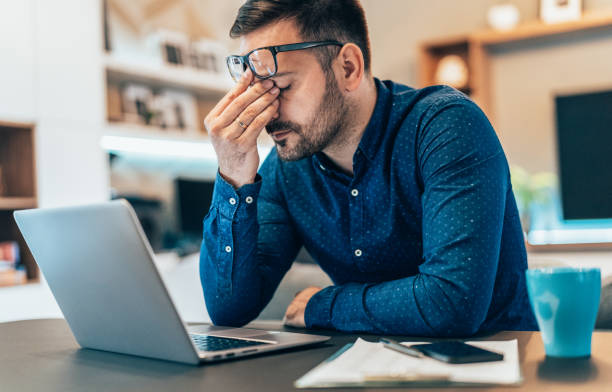 Tired Young Businessman Working At Home Using Lap Top And Looking Anxious